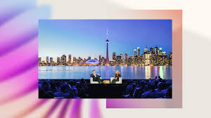 Two people on stage with a city skyline and water backdrop.